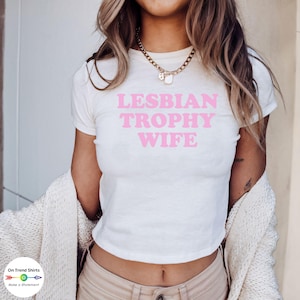 May include: White cropped t-shirt with the text "LESBIAN TROPHY WIFE" in pink letters.