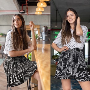 May include: A woman wearing a white and black polka dot blouse and a black and white circuit board print skirt. The skirt is a skater style with a flared hem.
