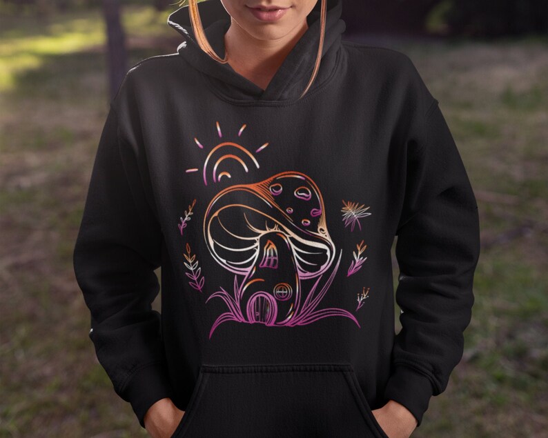 May include: Black hoodie with a graphic of a mushroom house with a rainbow sun and foliage. The mushroom is outlined in pink, orange, and yellow.