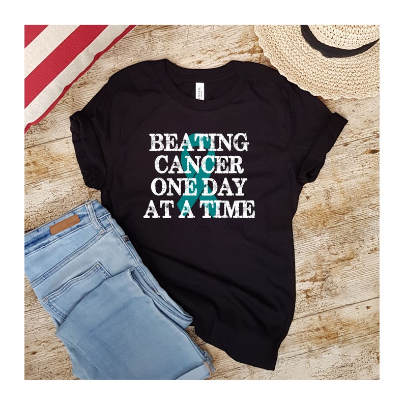 May include: Black t-shirt with the text "BEATING CANCER ONE DAY AT A TIME" in white with a teal ribbon graphic.