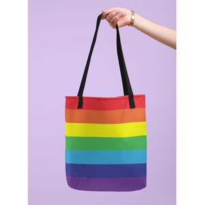 May include: A rainbow tote bag with black handles. The bag has six horizontal stripes in the colors of the rainbow: red, orange, yellow, green, blue, and purple.