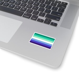 Puede incluir: Una pegatina de la bandera del orgullo gay con rayas azules, verdes y blancas en un port&aacute;til plateado.
