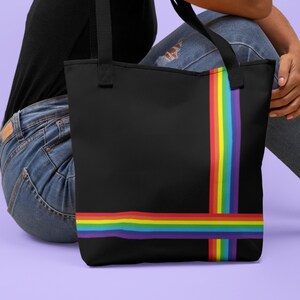 May include: Black tote bag with a vibrant rainbow stripe design. The bag features a vertical stripe on the right side and a horizontal stripe across the bottom, creating a colorful accent against the black background. The bag has black handles.