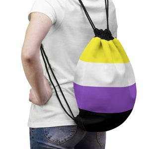 Pode incluir: Uma pessoa vestindo uma camiseta branca e jeans azul est&aacute; carregando uma mochila de cord&atilde;o com um design listrado amarelo, branco, roxo e preto.