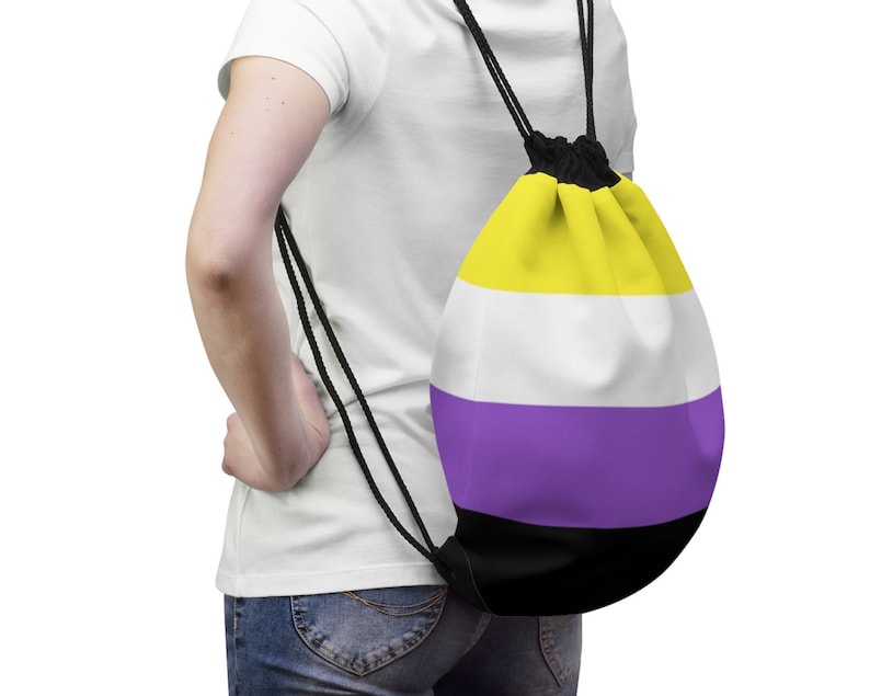 Pode incluir: Uma pessoa vestindo uma camiseta branca e jeans azul est&aacute; carregando uma mochila de cord&atilde;o com um design listrado amarelo, branco, roxo e preto.