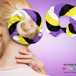 May include: A purple, white, yellow and black patterned hair scrunchie. The scrunchie is tied in a knot and is shown on a model's hair.