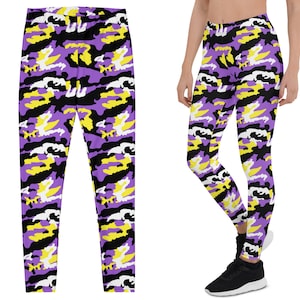 May include: Purple, black, yellow, and white camouflage leggings. The leggings are shown flat and on a person. The leggings have a high waist and a tight fit. The camouflage pattern is repeated throughout the leggings.