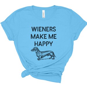 Puede incluir: Una camiseta azul claro con el texto "Wieners Make Me Happy" y una ilustraci&oacute;n en blanco y negro de un dachshund.