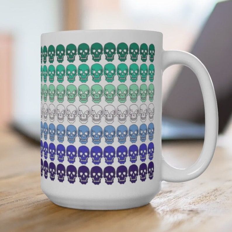 May include: White ceramic mug with a colorful pattern of skulls in shades of green, blue, and purple. The skulls are arranged in rows, creating a gradient effect.
