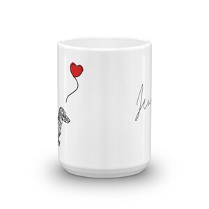 Puede incluir: Taza de cer&aacute;mica blanca con un dibujo de l&iacute;nea negra de un dachshund sosteniendo un globo rojo en forma de coraz&oacute;n. El texto "Jen" est&aacute; escrito en cursiva en el lado derecho de la taza.