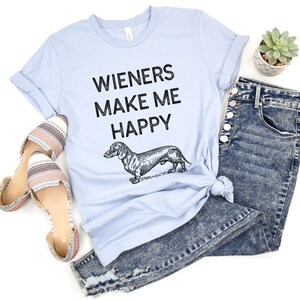 Puede incluir: Una camiseta azul claro con el texto "Wieners Make Me Happy" y una ilustraci&oacute;n en blanco y negro de un dachshund.