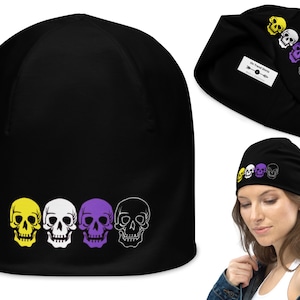 May include: Black beanie with four white skulls in a row. The skulls are outlined in yellow, white, purple, and white. The beanie has the text "Oh Nomad Shirts" on the side.