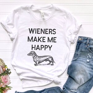 Puede incluir: Camiseta blanca con texto negro que dice "Wieners Make Me Happy" y una ilustraci&oacute;n en blanco y negro de un dachshund.