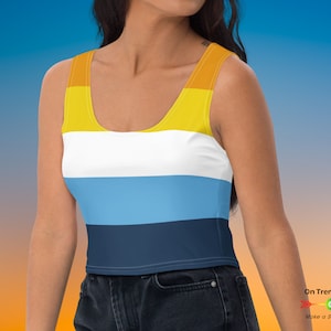 May include: A cropped tank top with horizontal stripes in yellow, white, light blue, and dark blue. The tank top is worn by a person with dark hair and is paired with dark blue jeans.