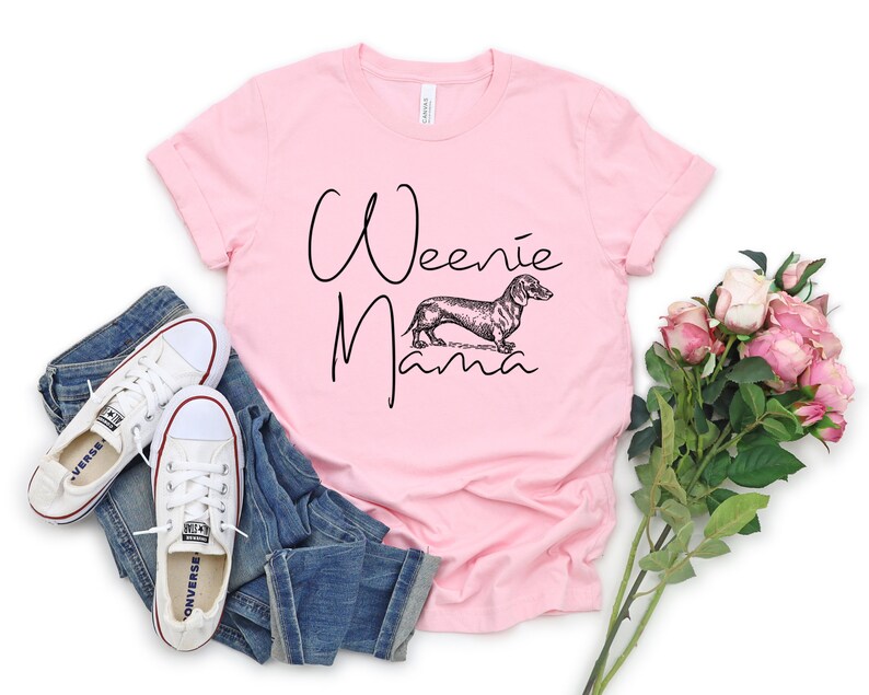 May include: Pink t-shirt with the text "Weenie Mama" in black script and a black and white illustration of a dachshund.