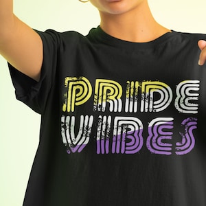 May include: Black t-shirt with the words "PRIDE VIBES" in a distressed, retro font. The text uses yellow, white, and purple colors, representing the non-binary pride flag. The shirt is a crew neck.
