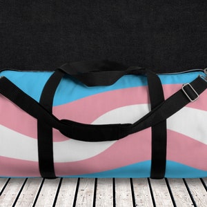 May include: A blue, pink and white striped duffel bag with black straps. The bag has a mesh pocket on the side.