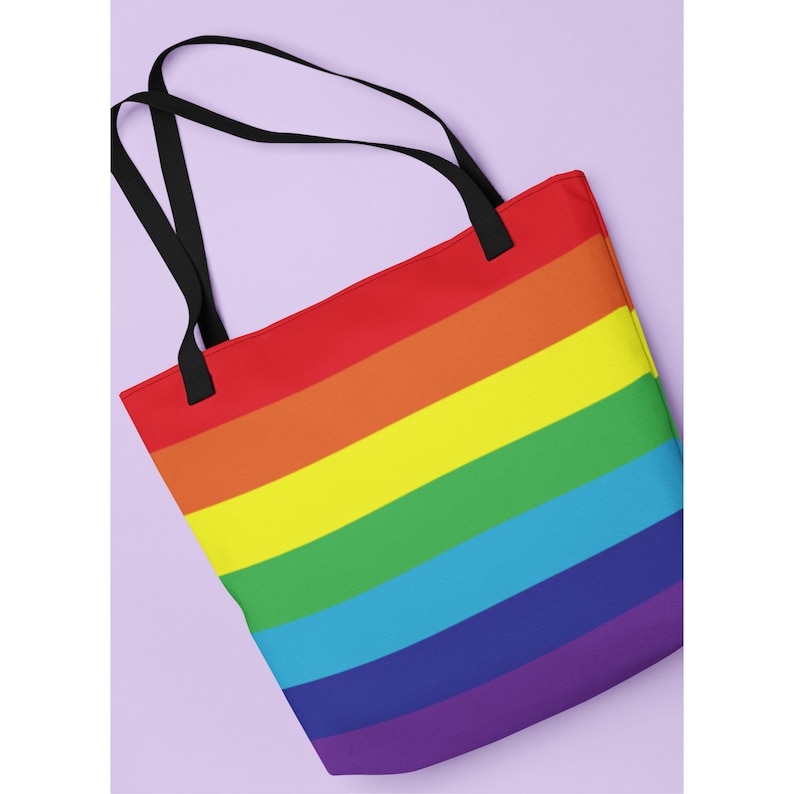 May include: A rainbow tote bag with black handles. The bag is made of canvas and features a rainbow design with red, orange, yellow, green, blue, indigo, and violet stripes.
