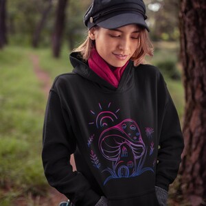 May include: A black hoodie with a pink and blue outline of a mushroom house with a sun and flowers. The hoodie has a drawstring hood.