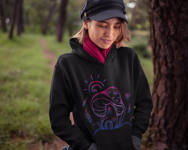 May include: A black hoodie with a pink and blue outline of a mushroom house with a sun and flowers. The hoodie has a drawstring hood.