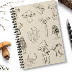 May include: A notebook with a spiral binding features a black and white illustration of various mushrooms. The notebook has a beige cover.