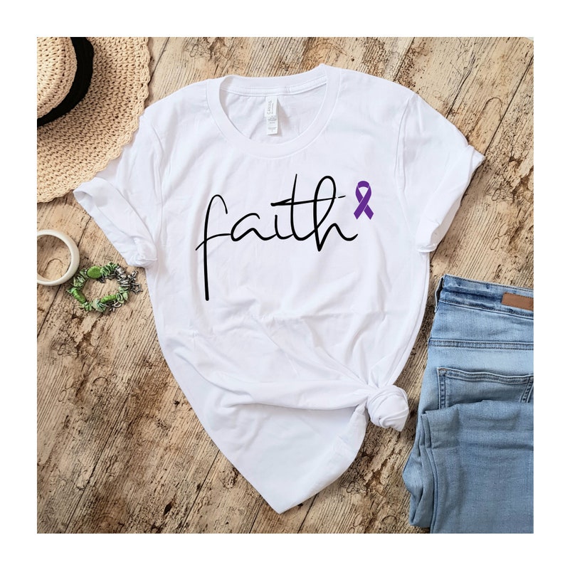 K&ouml;nnte beinhalten: Wei&szlig;es T-Shirt mit dem Wort "faith" in schwarzer Kursivschrift und einem lila Band.