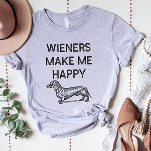 Puede incluir: Una camiseta gris con el texto "Wieners Make Me Happy" y una ilustraci&oacute;n en blanco y negro de un dachshund.