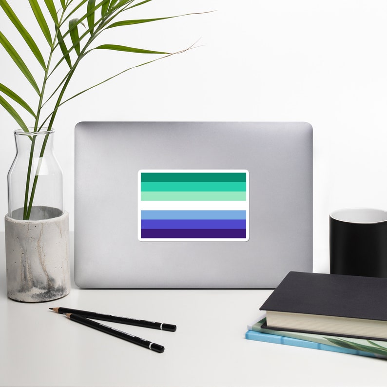 Puede incluir: Una pegatina con los colores verde, blanco y azul de la bandera del orgullo genderqueer. La bandera est&aacute; compuesta por cinco franjas horizontales: dos verdes, una blanca y dos azules.