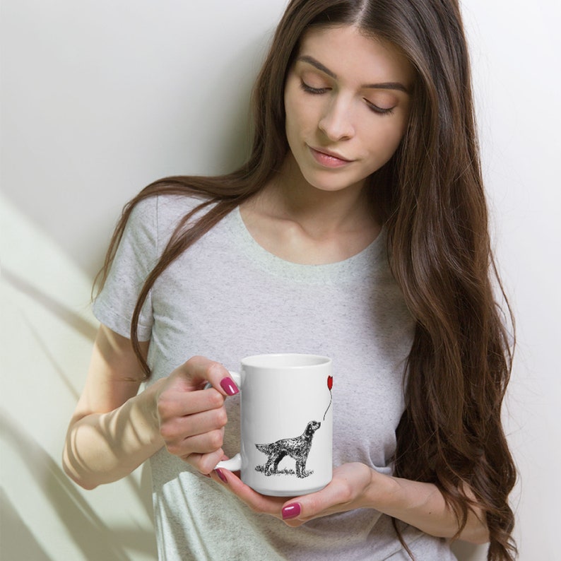 May include: White ceramic mug with a black and white illustration of a dog holding a red heart-shaped balloon. The dog is looking up at the balloon.