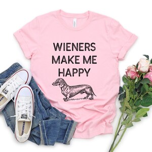 Puede incluir: Camiseta rosa con una ilustraci&oacute;n negra de dachshund y el texto "Wieners Make Me Happy".