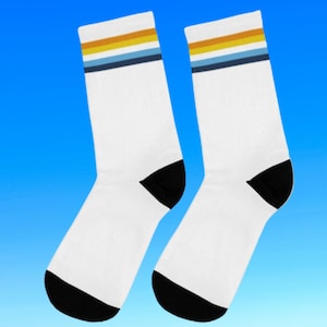 May include: A pair of white socks with black and blue stripes and a yellow stripe. The socks have a black heel and toe.