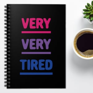 May include: A black spiral notebook with the words "VERY VERY TIRED" written in pink, purple, and blue. The words are separated by lines in the same colours.