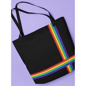 May include: Black tote bag with a rainbow stripe design. The bag features a solid black background with a vertical and horizontal rainbow stripe pattern. The bag has two black handles for carrying.