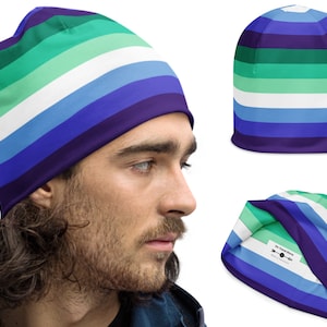 May include: A blue, green, and white striped beanie with a folded cuff. The beanie is made of a soft, stretchy fabric and features a subtle sheen. The beanie is shown on a person's head and laid flat.