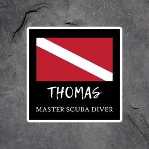 May include: A black and white sticker with a red scuba diving flag and the text "THOMAS MASTER SCUBA DIVER".
