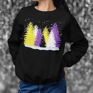 May include: Black sweatshirt featuring a design of three stylised pine trees in a snowy forest. The trees are coloured yellow, purple and white, representing the non-binary pride flag.