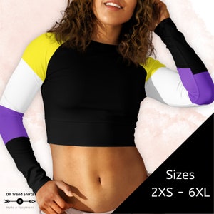 May include: A black, yellow, white, and purple long-sleeved crop top with a crew neck. The top has a color block design with the colors arranged in a horizontal stripe pattern on the sleeves. The text "Sizes 2XS - 6XL" is visible in the bottom right corner of the image.