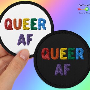 May include: Two round embroidered patches with the text "QUEER AF" in rainbow colors. The patches are on a white and black background.