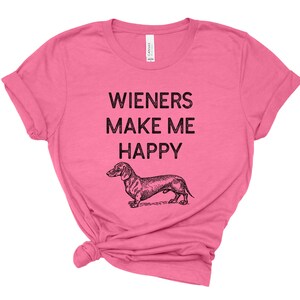 Puede incluir: Camiseta rosa con una ilustraci&oacute;n de dachshund y el texto "Wieners Make Me Happy".