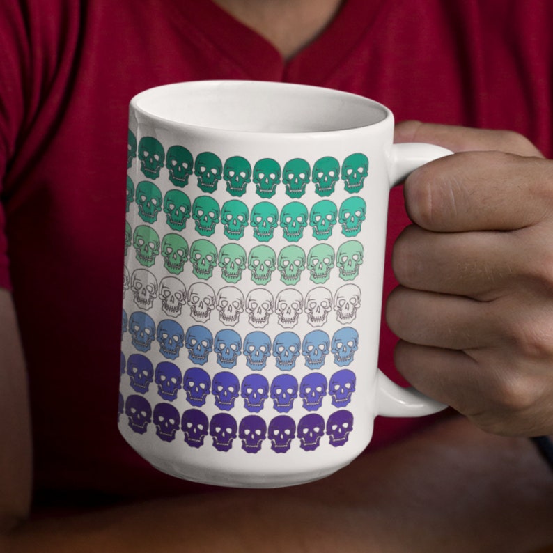 May include: White ceramic coffee mug with a colorful gradient pattern of skulls. The skulls are green, blue, and purple.