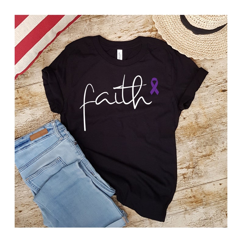 K&ouml;nnte beinhalten: Schwarzes T-Shirt mit dem Wort "faith" in wei&szlig;er Schrift und einem lila Band daneben.
