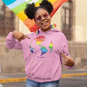 Pode incluir: Um moletom rosa com um gr&aacute;fico de globo terrestre arco-&iacute;ris na frente. A pessoa que est&aacute; usando o moletom est&aacute; sorrindo e apontando para o gr&aacute;fico.