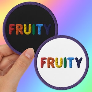 May include: Two round embroidered patches with a purple border. The word "FRUITY" is embroidered in rainbow colors on a black background on one patch and on a white background on the other patch.
