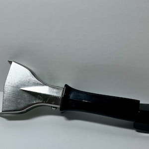 May include: A metal pot handle lifter with a black plastic handle. The lifter has a silver-coloured, angled head with a pointed tip. The handle is rectangular and tapers to a flat end.