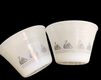 May include: Two white ceramic bowls with a gray swan design. The swans are outlined in black and have orange beaks. The bowls have a white background and a gray rim.