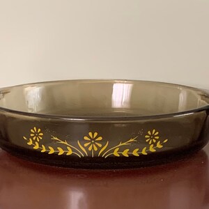 May include: A brown glass baking dish with a yellow floral design. The dish has two handles on the sides.