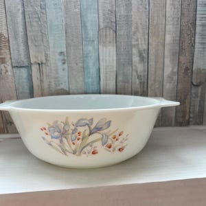 May include: White ceramic baking dish with a floral design featuring blue irises and red berries. The dish has two handles on the sides.