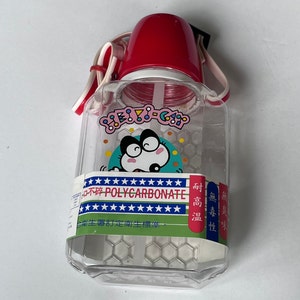 May include: A clear plastic water bottle with a red lid and a cartoon character on the front. The bottle has a strap and says "POLYCARBONATE" on the side. The bottle is on a white background.