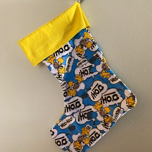 May include: A blue and white Christmas stocking with a yellow cuff. The stocking features a cartoon character with the words "D'oh!" and "Woo-Hoo!" repeated throughout the design.
