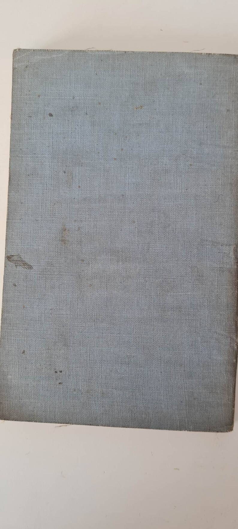 May include: A light blue book cover with a textured fabric surface. The cover has a few small brown spots.